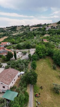 Vertical aerial drone view of countryside houses nestled among green rolling hills and olive trees in Staiano near Teramo in Abruzzo region Italy.