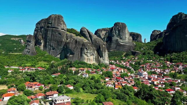 Aerial view of the Meteora rock formations rising above the village of Kastraki with lush green trees and clear blue sky in Greece.