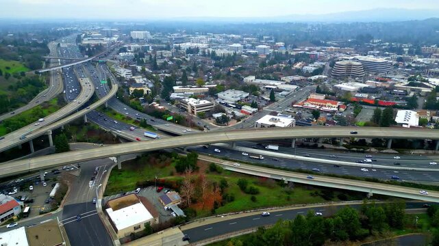 Aerial view of a complex highway interchange with multiple lanes and overpasses surrounded by urban buildings and greenery in San Francisco, California, United States.