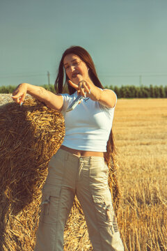 A vintage snapshot captures a teenage girl celebrating freedom in a sun-drenched hayfield. She's dancing with pure joy, lost in the music and the natural beauty of the summer countryside. Soft lens fl