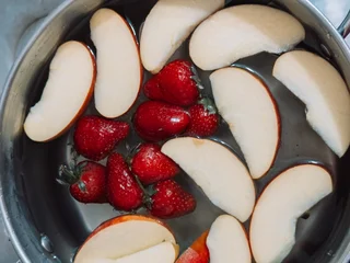 Fresh strawberries and sliced apples in a pot with water prepared for cooking homemade fruit compote in home kitchen. © Anastassiya 