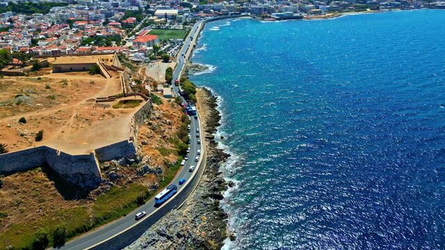 Aerial view of the historic Fortezza of Rethymno overlooking the Mediterranean Sea with a coastal road and vehicles in Crete, Greece.