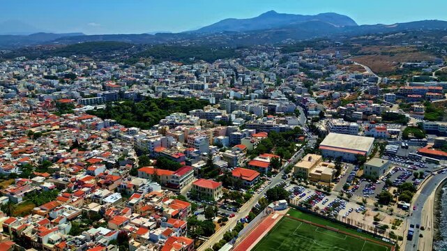 Aerial view of the coastal city of Rethymno with its dense urban layout, red-tiled roofs, and proximity to the Mediterranean Sea in Crete, Greece.