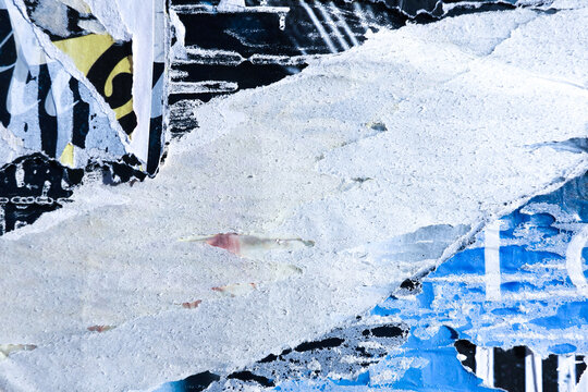 Textured surface with layers of old torn paper posters and paint. Blue, black, and white colors placard pieces on wall