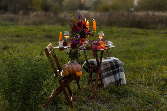 Cozy autumn table decoration for a thanksgiving party outdoors. Grapes, fig, rose wine, candles, pumpkins as decor. Elegant wedding fall arrangement, beautiful setting for a romantic proposal