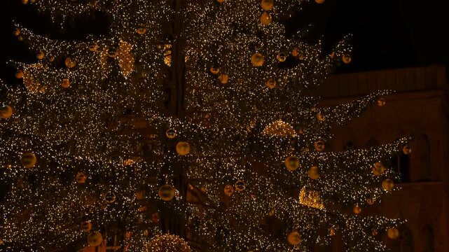 Christmas tree sparkling with golden lights at night. Magnificent christmas tree decorated with thousands of twinkling golden lights and shiny baubles standing in a city square at night