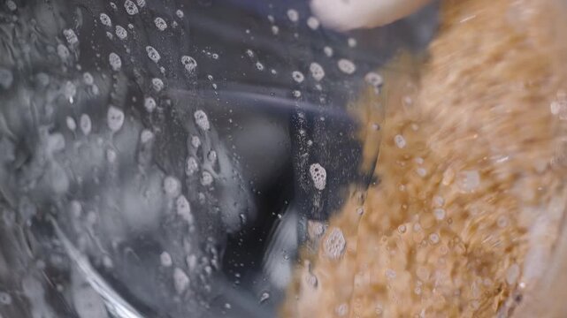 Washing machine drum cleaning a teddy bear toy. Detailed close-up of a brown teddy bear spinning inside a washing machine drum during a cleaning cycle, with soapy water and bubbles surrounding