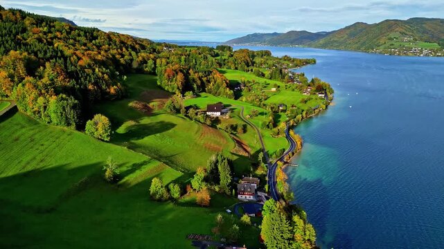 Aerial view of Attersee lake with lush green meadows, autumn-colored trees, and houses along the shoreline in Vocklabruck District, Upper Austria, Austria.
