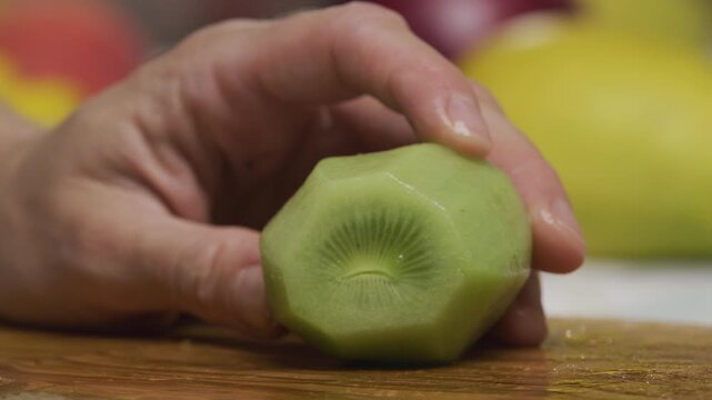 Woman's hand holding shaved kiwi and slicing it with large knife - slow motion