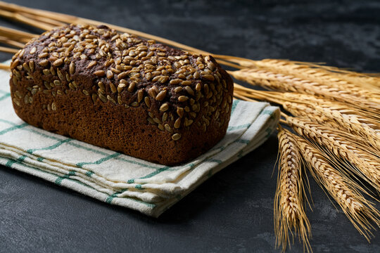 loaf of freshly baked wholemeal rye bread with sunflower seeds on dark kitchen table, selective focus.
