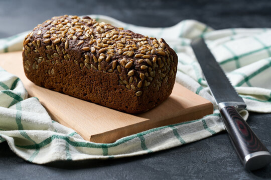 wholemeal rye bread with sunflower seeds on dark kitchen table, selective focus.