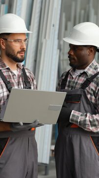 Diverse industrial workers discussing project on laptop in warehouse