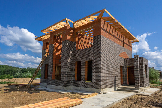 Construction of a modern brick house with open roof framing taken on a sunny day in a residential area