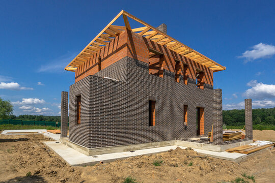 Brick and wood house under construction with blue sky and clouds in the background