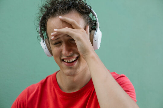 Smiling young man with hand on forehead showing shy expression.