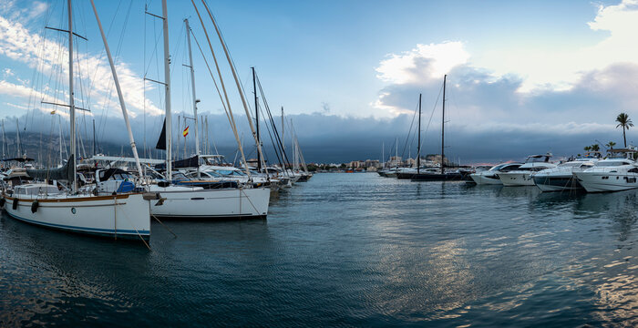 Panoramic view of sailboats and motor yachts at harbor during golden hour with sunlight reflecting on water