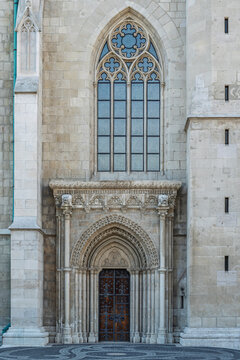 Carved Gothic entrance portal and wooden door beneath a tracery rose window on the facade of Matthias Church in Budapest, Hungary