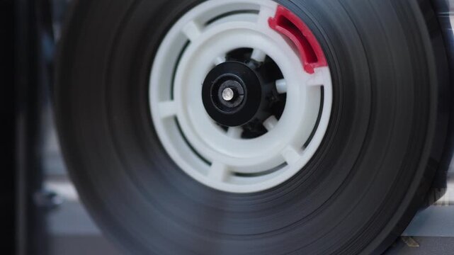 Macro shot of a spinning white cassette reel with magnetic tape on an analog recorder deck. Vintage audio equipment playing music in close-up detail
