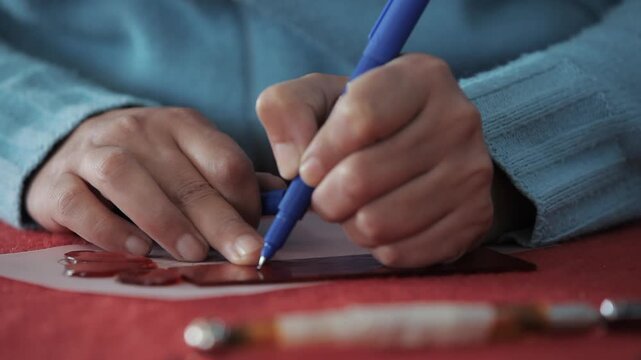 Close-up of hands using a blue pen to carefully trace a pattern onto a dark material. Handmade craft, artistic hobby, precision work, and creative DIY project concept.