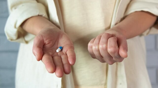 Person offering a choice between two different pills. Hands opening to reveal two different colored pills, one blue and one orange, offering a difficult choice or decision between two distinct options