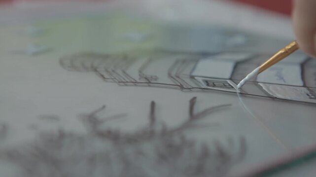 Close-up of a hand using a fine brush to apply white paint onto a glass surface. Glass painting art, creative hobby, and DIY craft concept.