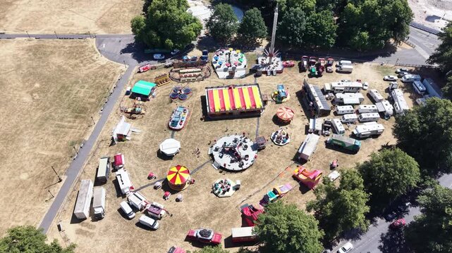 Aerial view of a traveling funfair and amusement park set up in a green city park on a sunny day