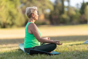 Fotobehang Lotusbloem Senior woman doing yoga meditation in lotus pose outdoors  © KONSTANTIN SHISHKIN