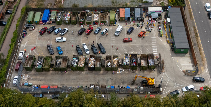 Aerial view of Stevenage Recycling Centre with rows of waste skips, parked cars, and an excavator in a busy waste management facility in Stevenage, England, United Kingdom.