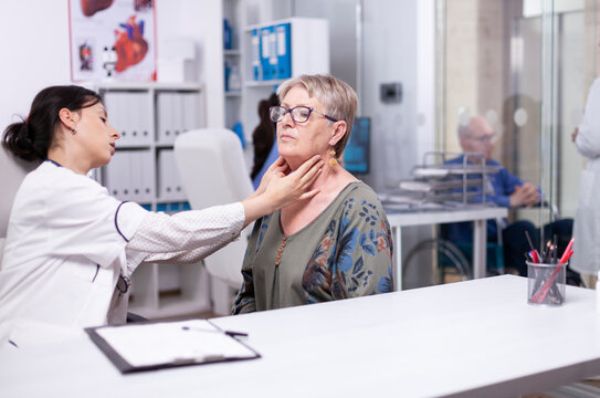 Professional physician palpates an elderly woman's neck lymph nodes during a clinic examination for thyroid, throat and treatment assessment.
