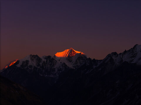 Aerial view of a snow-capped Himalayan mountain peak illuminated by the warm golden light of sunrise against a dark twilight sky in Nepal.