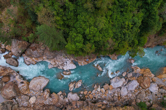 Aerial view of a turquoise river with white rapids flowing through a rocky gorge surrounded by a lush green forest in Nepal.