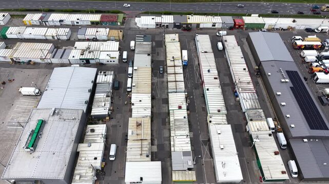 Aerial view of a bustling farmers market with numerous colorful vendor stalls, trucks, and vehicles parked, showcasing a vibrant scene of fresh produce and local goods