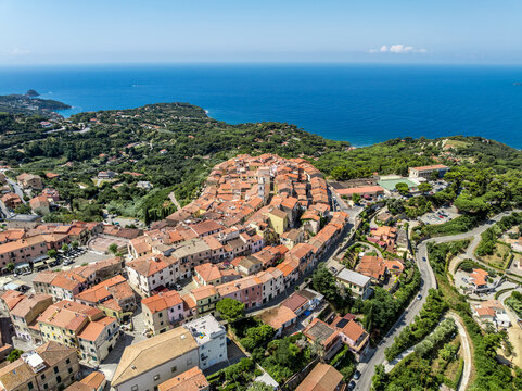 Aerial view of the historic hilltop town of Capoliveri with dense terracotta rooftops and narrow streets surrounded by lush vegetation overlooking the sea in Capoliveri, Tuscany, Italy.