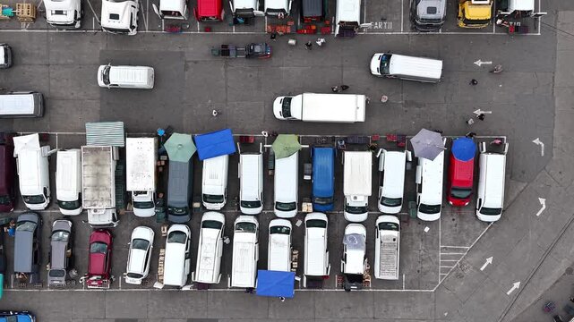 Aerial view of busy farmers market with trucks and vans parked along street. Vibrant produce and bustling activity among vendors and customers. Lively atmosphere of shoppers engaging for fresh produce