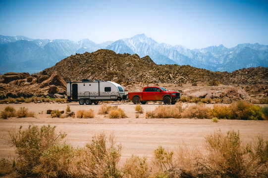 Red pickup truck towing travel trailer in Alabama Hills with Sierra Nevada mountains, California