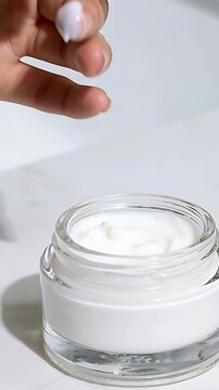 Vertical video: Pressing finger into glass jar on white table, swirling cream testing on finger tip