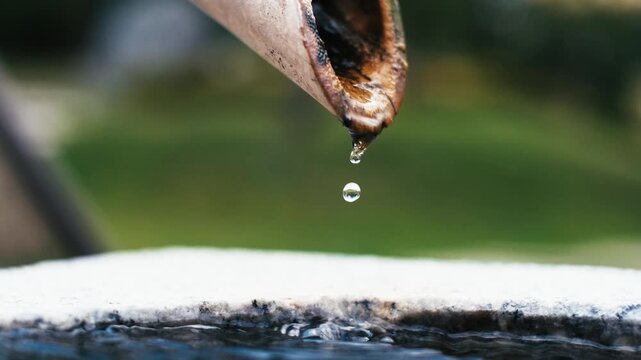 Calm water dripping from bamboo pipe into stone bowl, close up