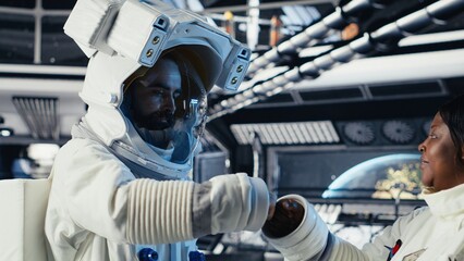 Astronaut puts on a helmet and shares a fist bump with a colleague before leaving the space station for scheduled planetary mission operations. © DC Studio