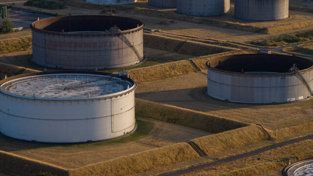 Aerial view of Tanklager oil storage tanks surrounded by grassy embankments in the golden hour light in Hunxe, North Rhine-Westphalia, Germany.