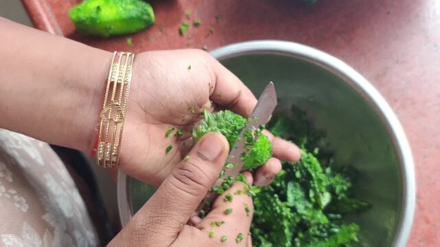 Hands of a person peeling and scraping bitter gourd skin into a stainless steel bowl with a knife close up shot