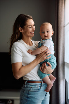 Cute baby boy looking at camera while mother is holding him at home.