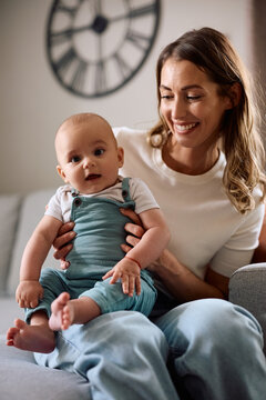 Cute baby boy and his mother sitting on sofa at home.