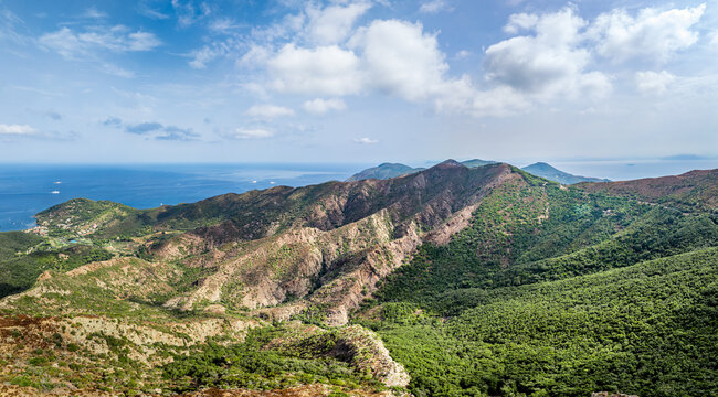 Aerial view of the landscape surrounding Castello del Volterraio, with green hills, rocky ridges, and the blue sea in the background in Portoferraio, Toscana, Italy.