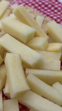 Raw French Fries French-Cut Potatoes on Red Plaid Background 4K. High-angle shot of freshly cut, raw potato sticks prepared for French fries, piled on a traditional red and white checkered tablecloth.