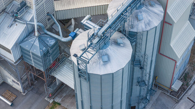 Aerial view of galvanized grain silos, conveyor bridges, and processing equipment at a modern agricultural storage facility in Le Pouzin, Auvergne-Rhone-Alpes, France.