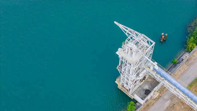 Aerial view of an industrial bulk loading tower with an enclosed conveyor system situated on the turquoise waters of the Rhone River in Le Pouzin, Auvergne-Rhone-Alpes, France.