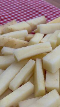 Raw French Fries French-Cut Potatoes on Red Plaid Background 4K. High-angle shot of freshly cut, raw potato sticks prepared for French fries, piled on a traditional red and white checkered tablecloth.