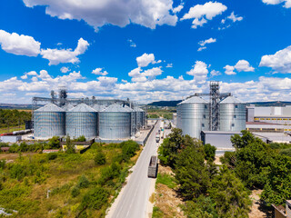 Large industrial facility with silos located near a road under a blue sky filled with clouds in a rural area © DSMT