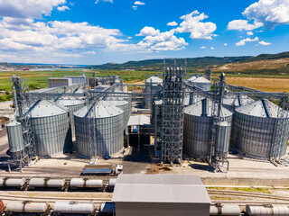 Grain storage facility located near a railway with silos and equipment under a blue sky © DSMT