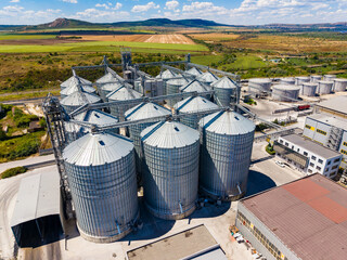 Grain storage silos in a rural area with fields and distant hills during daylight hours © DSMT